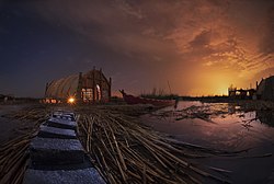 Mesopotamian Marshes at night, southern Iraq. A reed house (Mudhif) and a narrow canoe (Mashoof) are in the water. Mudhif structures have been one of the traditional types of structures, built by the Marsh people of southern Mesopotamia for at least 5,000 years. A carved elevation of a typical mudhif, dating to around 3,300 BC was discovered at Uruk.[18]