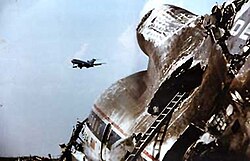 Wreckage of Delta Air Lines Flight 191 tail section after a microburst slammed the aircraft into the ground. Another aircraft can be seen flying in the background past the crash scene.