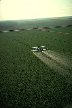 A crop-duster spraying pesticide on a field