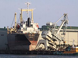 A damaged crane stands next to a ship lifted onto the docks at Sendai's port.