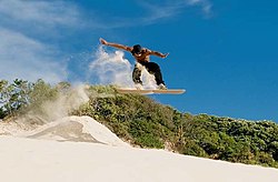 A sandboarder does a jump on Florianópolis dunes.
