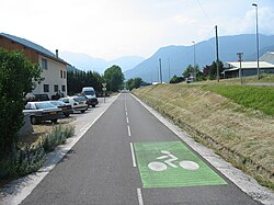 On-road bike lane in France marked with a bicycle symbol and white lines, running alongside a residential road with mountains in the background.