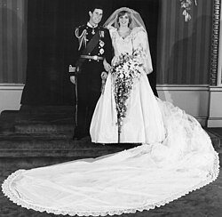 The smiling couple in formal attire. The bride wears a gown with a long train and holds a large bouquet, standing beside the groom in a military uniform adorned with medals.