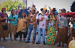 Indigenous protesters are standing wearing traditional garments along with "common" clothes