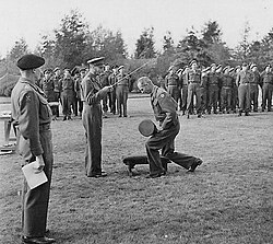 Lieutenant General Miles Dempsey is invested with his knighthood as Knight Commander of the Order of the Bath, in the field of battle, by King George VI on 15 October 1944, while Field Marshal Sir Bernard Montgomery looks on.
