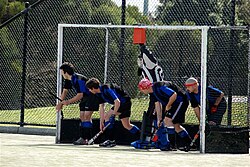 A group of five defenders, including the goalkeeper, prepare on the back line for a short corner.