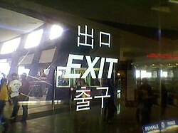 Multilingual sign at an exit of SM Mall of Asia in Pasay, Philippines. Three or four languages are shown: Japanese/Mandarin Chinese ("deguchi" or "chūkǒu", respectively), English ("exit") and Korean ("chulgu"). While Filipinos themselves are anglophones, such signs cater to the growing number of Koreans and other foreigners in the country.