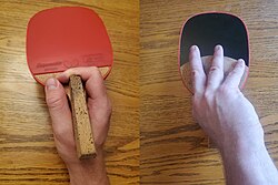 The forehand (red) and back side (black) view of a Japanese/Korean Penhold grip. The back side has no rubber and is not used for play, and so the fingers are extended over it for better feeling of the ball.