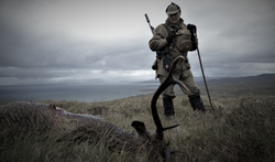 Professional deerstalker standing over a downed red stag in Scotland