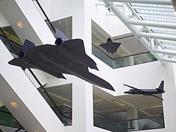 Suspended from the ceiling of the glass-enclosed atrium: three models of the U-2, Lockheed A-12, and D-21 drone. These models are exact replicas at one-sixth scale of the real planes. All three had photographic capabilities. The U-2 was one of the first espionage planes developed by the CIA. The A-12 set unheralded flight records. The D-21 drone was one of the first crewless aircraft ever built. Lockheed Martin donated all three models to the CIA.