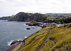 The South West Coast Path passes along the cliffs (seen in the distance) at Ilfracombe, North Devon. The highest point in this view is Hillsborough (447 feet, 136 metres). Part of Ilfracombe is seen on the right.