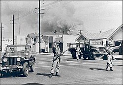 Soldiers direct traffic away from an area of South Central Los Angeles burning during the 1965 Watts riots.