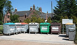 A recycling point in New Byth, Scotland, with separate containers for paper, plastics, and differently colored glass