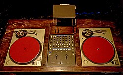 Analog and digital 2010s DJ station. A Rane Sixty-Two DJ mixer is placed between two Technics SL-1200 turntables with a laptop.