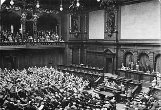 Members of the Nazi Party can be seen seated in the Reichstag in the left foreground, the far-right seats from the speakers point of view.