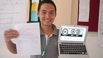 The logo on the computer screen is a Creative Commons license, while the paper explains (in Khmer) that the image is open content.