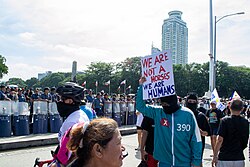 Filipino protester in Squid Game cosplay holding a picket sign showing the divide between protestors and the political elite during the Asian Spring.