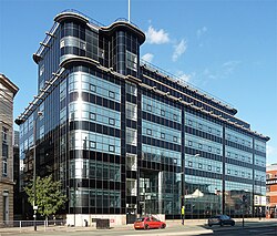 An art deco glass and steel building that is largely built from cuboids joined together, some of which have rounded corners. The photograph is taken on a sunny day from across the street.