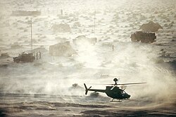 An OH-58D Kiowa helicopter departs from a communications site in the desert during Operation Desert Shield