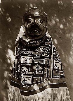 Woman with mask, wearing a chilkat blanket.