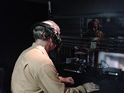 An audio describer working in a live theater. A small mixer and transmitter are visible, and the lit stage can be seen in the distance.