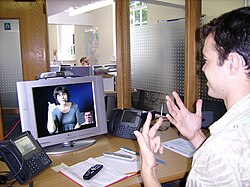 A deaf or hard-of-hearing person uses a Video Relay Service at his workplace to communicate with a hearing person in London (2007).