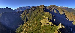 Machu Picchu peak, ruins and modern roead with Andean mountain backdrop.