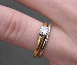 A white gold wedding ring and a single-diamond, gold-banded engagement ring. In many cultures, wives show their marital status through various symbols.