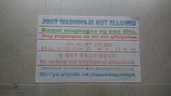 Multilingual message at a public toilet in Puerto Princesa, Palawan, Philippines that prohibits foot washing. Text is written in six languages: English, Filipino, Cebuano, Chinese, Korean, and Russian, from top to bottom.