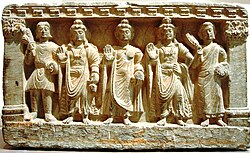 stone statue group, a Buddhist triad depicting, left to right, a Kushan, the future buddha Maitreya, Gautama Buddha, the bodhisattva Avalokiteśvara, and a Buddhist monk. 2nd–3rd century. Guimet Museum