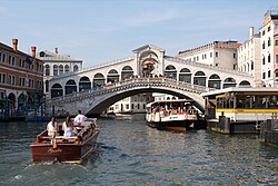 A white bridge, covered with a roof, passing over a canal with buildings on both sides