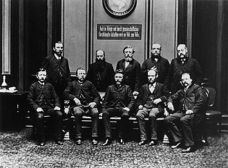 SPD members in Reichstag 1889. Sitting from left to right: Georg Schumacher, Friedrich Harm, August Bebel, Heinrich Meister and Karl Frohme. Standing: Johann Heinrich Wilhelm Dietz, August Kühn, Wilhelm Liebknecht, Karl Grillenberger, and Paul Singer.