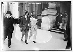 Upton Sinclair wearing a white suit and black armband, picketing the Rockefeller Building in New York City