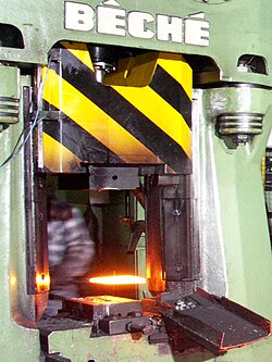 A red-hot metal workpiece is inserted into a forging press.