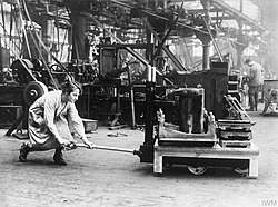 A worker at Bowling Iron Works, England, using an early pallet jack to lift a skid weighing 10 long hundredweight (1,120 lb; 508 kg), 1918