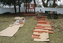 A playground being built for a homeowner's backyard as part of a handyman project. Modern playgrounds can have many options besides swingsets, including sandboxes, rope-climbs, tic-tac-toe games, a fort with dormer roofs and a chimney, a slide, and other amenities.