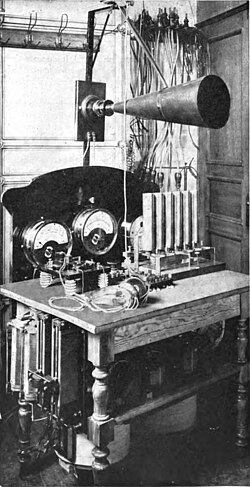 One of the crude pre-vacuum tube AM transmitters, a Telefunken arc transmitter from 1906. The carrier wave is generated by 6 electric arcs in the vertical tubes, connected to a tuned circuit. Modulation is done by the large carbon microphone (cone shape) in the antenna lead.