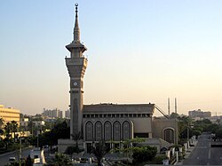 The front side of a mosque with only one minaret containing a clock.