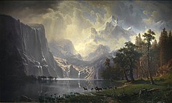 Painting of a lake with deer at the water's edge and the Sierra Nevada in the background. Light is shining between the clouds onto the mountains.