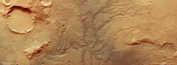 An orange moonscape, showing the rusty Mars soil. Impressions in the sand show where rivers once flowed, in a fractal-like form.