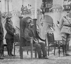 The Coronation of Faisal as King of Iraq. Faisal seated, to his right are British High commissioner Percy Cox and Lieutenant Kinahan Cornwallis, to his left commander-in-chief of all British troops in the Mesopotamia Commander General Aylmer Haldane.[17]