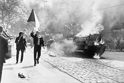 Czechoslovak protestors carrying their national flag past a burning Soviet tank in Prague, 1968