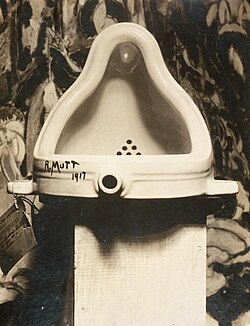 The original Fountain by Marcel Duchamp, 1917, photographed by Alfred Stieglitz at the 291 after the 1917 Society of Independent Artists exhibit. Stieglitz used a backdrop of The Warriors by Marsden Hartley to photograph the urinal. The exhibition entry tag can be clearly seen.[154]