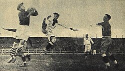 An action shot from a football match. A goalkeeper jumps and catches the ball