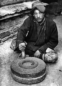 Tibetan operating a quern (1938). The upright handle of such rotary handmills, set at a distance from the centre of rotation, works as a crank.[1][2]