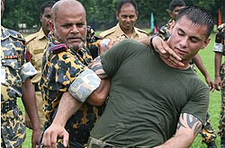 A Bangladesh Rifles (now Border Guard Bangladesh) Senior Warrant Officer (left in yellow/green outfit) applies a mechanical advantage control/hold to a US Marine during training.