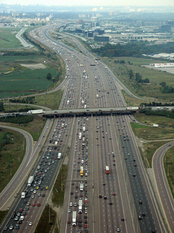 401 highway near Toronto, Canada with a suburban industry area in the background. Note the office buildings are far apart. Many office buildings in suburban industry areas stand on large green campuses, unlike downtown ones with nearby buildings and very little greenery.